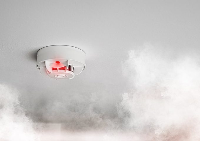 Un rilevatore di fumi antincendio in azione in mezzo a una nuvola di fumo bianco in una stanza con soffitto chiaro