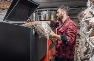 Un ragazzo con la barba svuota un sacco di pellet dentro a una caldaia