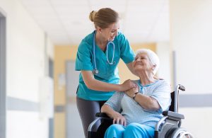 Un'infermiera di una casa di riposo parla allegramente con una donna anziana sorridente seduta su una sedia a rotelle