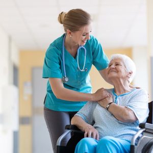 Un'infermiere di una casa di riposo parla allegramente con una donna anziana sorridente seduta su una sedia a rotelle