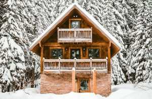 Una baita di montagna in legno in un panorama innevato con alberi dietro alla casa