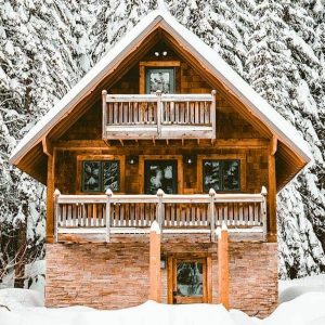 Una baita di montagna in legno in un panorama innevato con alberi dietro alla casa