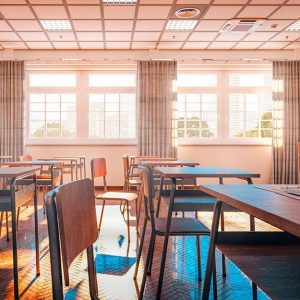 Un'aula scolastica vista di lato, senza alunni ma con banchi, cattedra, lavagna (su cui sono scritte formule matematiche) e finestra da cui entra la luce