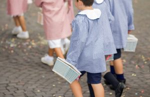 Dei bambini di una scuola elementare di Asti stanno andando a scuola con i grembiuli blu e rossi e con il cestino in mano