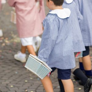 Dei bambini di una scuola elementare di Asti stanno andando a scuola con i grembiuli blu e rossi e con il cestino in mano