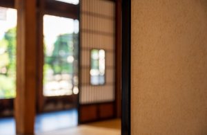 Dettaglio di una casa in caratteristico stile giapponese, con in primo piano una parete di carta e, sullo sfondo, sfocato, il resto dell'ambiente