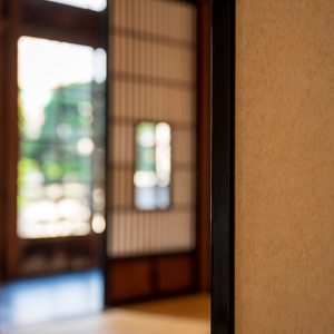 Dettaglio di una casa in caratteristico stile giapponese, con in primo piano una parete di carta e, sullo sfondo, sfocato, il resto dell'ambiente