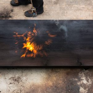 Un uomo che tiene in mano una torcia e brucia un grosso pezzo di quercia creando fiamme e fumo, secondo l'antica tecnica giapponese dello