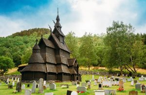 La Stavkirke di Borgund, in Norvegia, tra le lapidi del cimitero circostante e un rilievo boscoso sullo sfondo