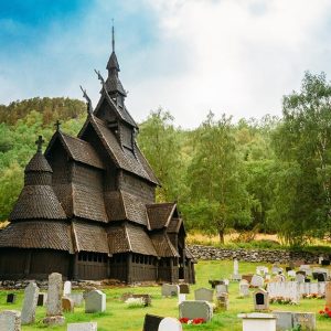 La Stavkirke di Borgund, in Norvegia, tra le lapidi del cimitero circostante e un rilievo boscoso sullo sfondo