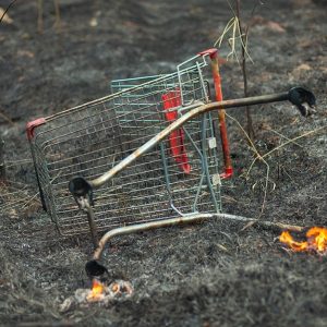 Un carrello della spesa rotto e in fiamme su un campo bruciato