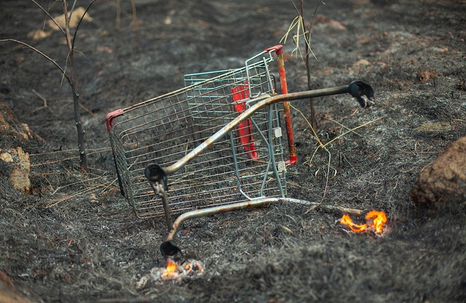 Un carrello della spesa rotto e in fiamme su un campo bruciato