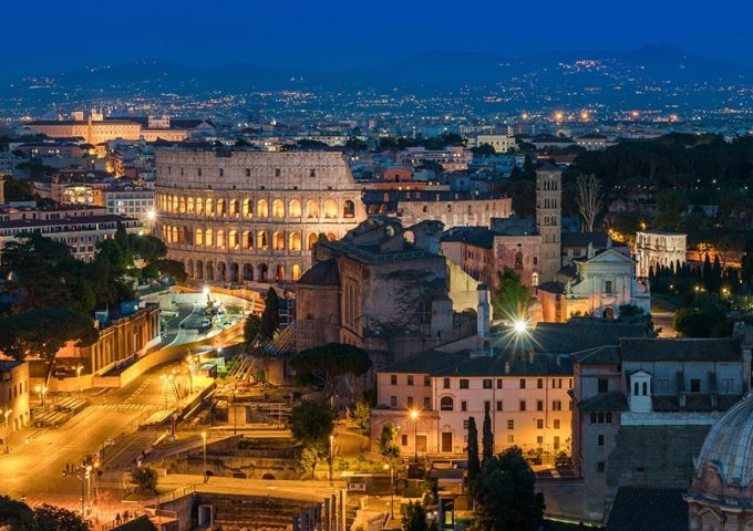 Roma, di sera, illuminata e vista dall'alto, con il Colosseo al centro dell'immagine