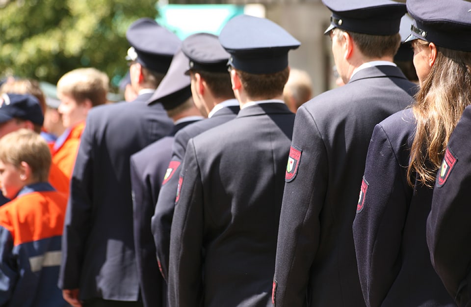 Una delegazione di pompieri tedeschi visti di spalle, in fila, mentre passa durante un evento pubblico