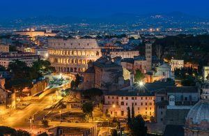 Roma, di sera, illuminata e vista dall'alto, con il Colosseo al centro dell'immagine