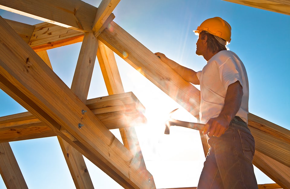 Un operaio sta lavorando alla struttura in legno di un tetto con il sole al centro della foto