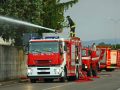 Dei mezzi dei Vigili del Fuoco vicino al recinto in cemento di un'edificio con un pompiere che sta sparando acqua da un cannoncino sul tetto di uno dei camion