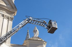 Dei Vigili del Fuoco all'interno del cestello di un'autoscala in prossimità di una chiesa