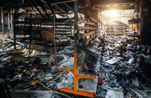L'interno distrutto di una fabbrica andata a fuoco, con in primo piano i resti di uno scaffale in metallo