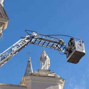 Dei Vigili del Fuoco all'interno del cestello di un'autoscala in prossimità di una chiesa