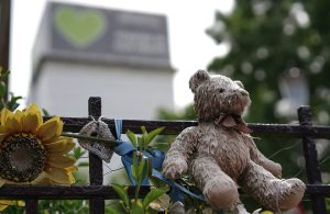 Un cancello nei pressi della Grenfell Tower, che si vede sullo sfondo, con fiori e oggetti in ricordo delle vittime