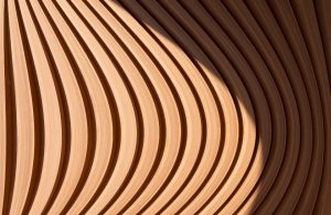 Dettaglio ravvicinato di una struttura in legno incurvato di un edificio, con giochi d'ombre che sembrano formare un motivo astratto