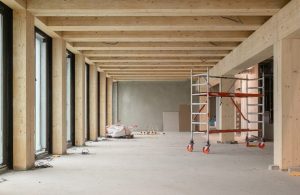 L'intero di un open space di uffici in costruzione: la struttura è formata da grandi travi in legno e sul pavimento ci sono attrezzi, materiali e un ponteggio mobile
