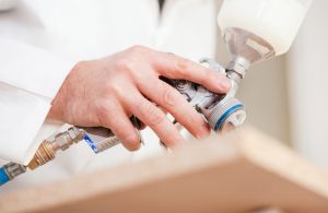 La mano di un uomo con camice bianco che sta spruzzando della vernice ignifuga su un'asse di legno