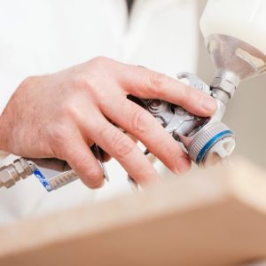 La mano di un uomo con camice bianco che sta spruzzando della vernice ignifuga su un'asse di legno