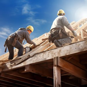 Due operai edili stanno lavorando in una giornata serena sulla struttura in legno di un tetto di un edificio in costruzione