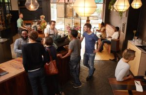 Vista dall'alto dell'interno di una caffetteria in stile anglosassone con bancone, baristi, clienti e tavoli