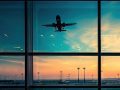 La vetrata di un aeroporto con luce drammatica all'alba o al tramonto, con un aereo che sta decollando