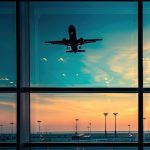 La vetrata di un aeroporto con luce drammatica all'alba o al tramonto, con un aereo che sta decollando