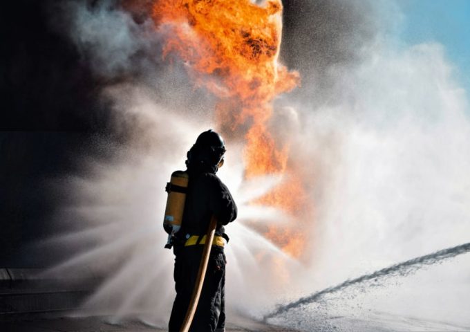 Un pompiere visto di spalle sta cercando di domare un incendio con un getto d'acqua