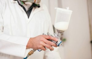 Un uomo con tuta bianca e volto non visibile sta applicando a spruzzo della vernice ignifuga