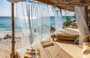 Lussuosi lettini matrimoniali con tetto in paglia, sulla spiaggia di una villaggio turistico affacciato sul mare