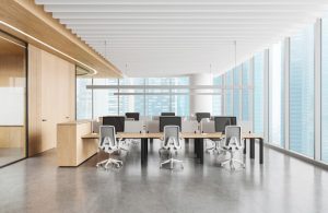 Un ufficio open space vuoto con grande scrivania e diverse postazioni con computer, grandi finestre, ingresso rivestito in legno