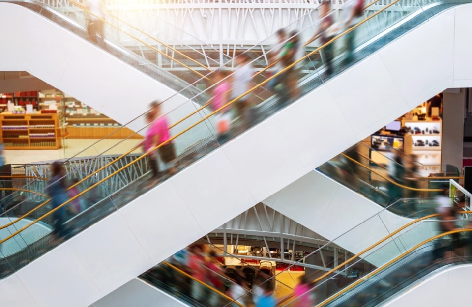 Vista laterale dell'incrocio tra due scale mobili, in un centro commerciale, con alcune persone sfocate per dare senso di movimento