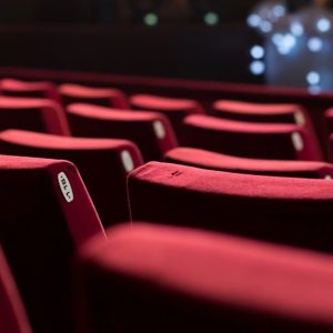 Alcune poltrone rosse e vuote di un cinema, con una porzione di schermo visibile